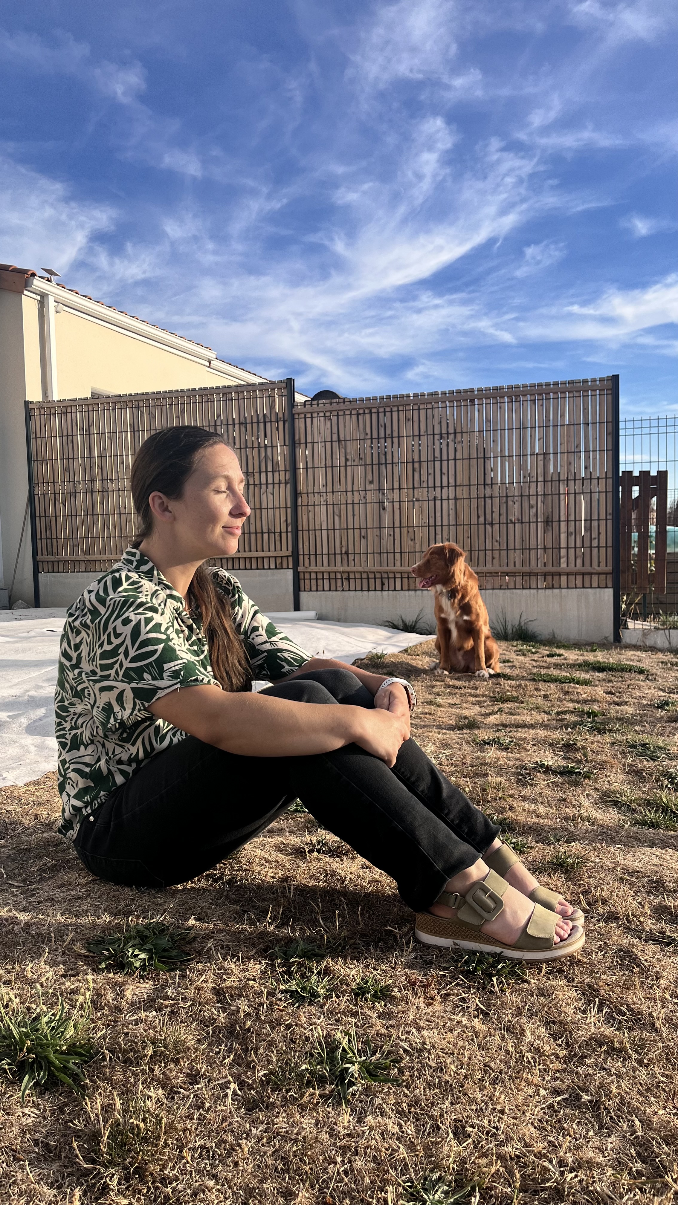 Alexia profite d’un moment calme dehors, avec son chien à l’arrière-plan